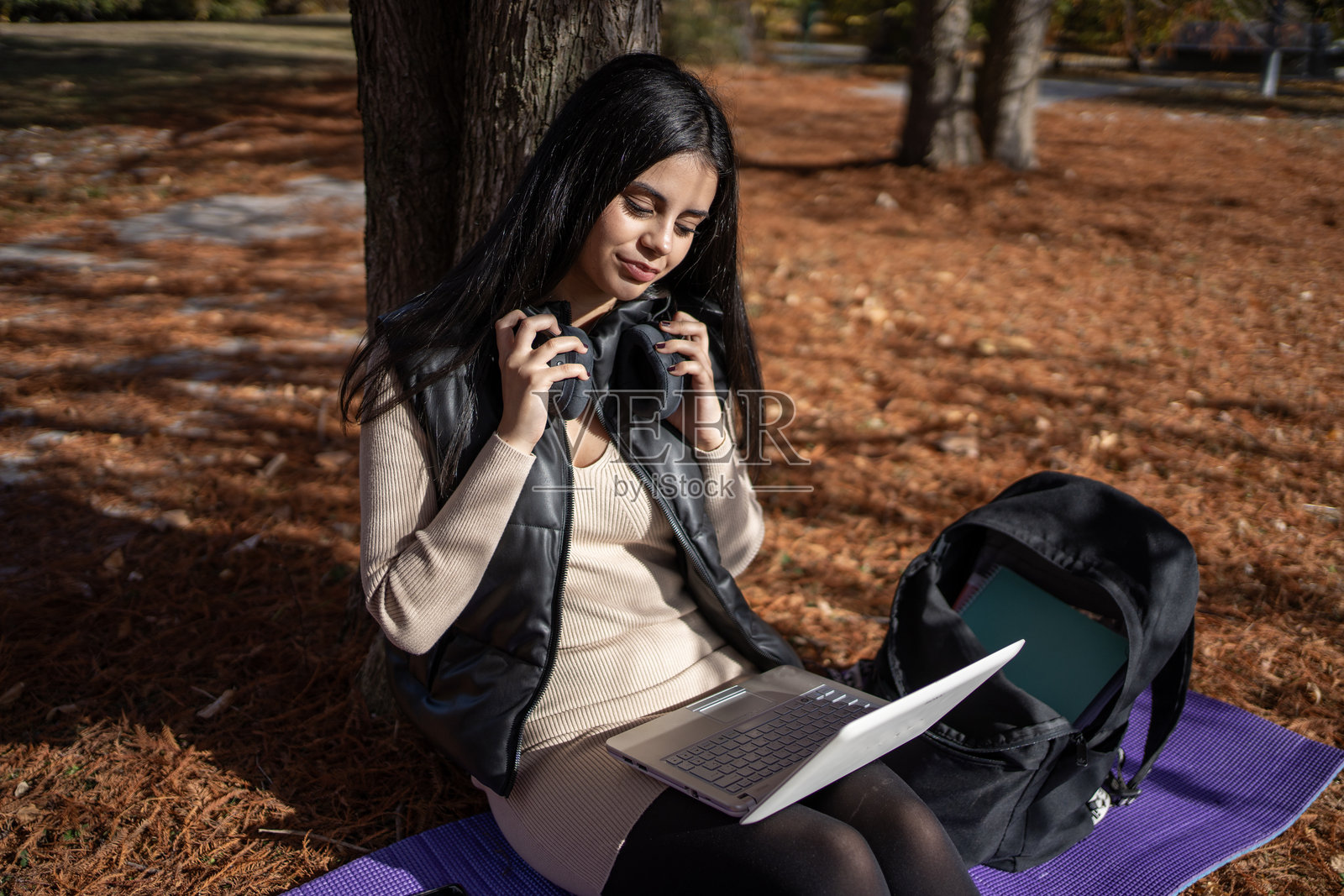 年轻女性在秋天的公园里戴着耳机使用笔记本电脑照片摄影图片
