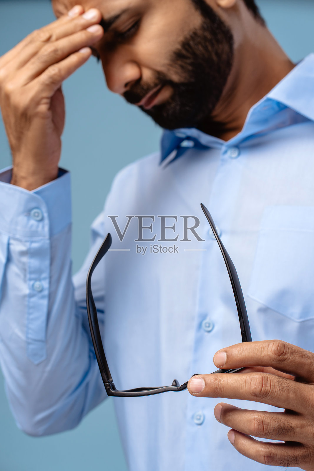 一位中年印度男子面露不快，双眼闭合，手握眼镜，似乎正在忍受头痛。照片摄影图片