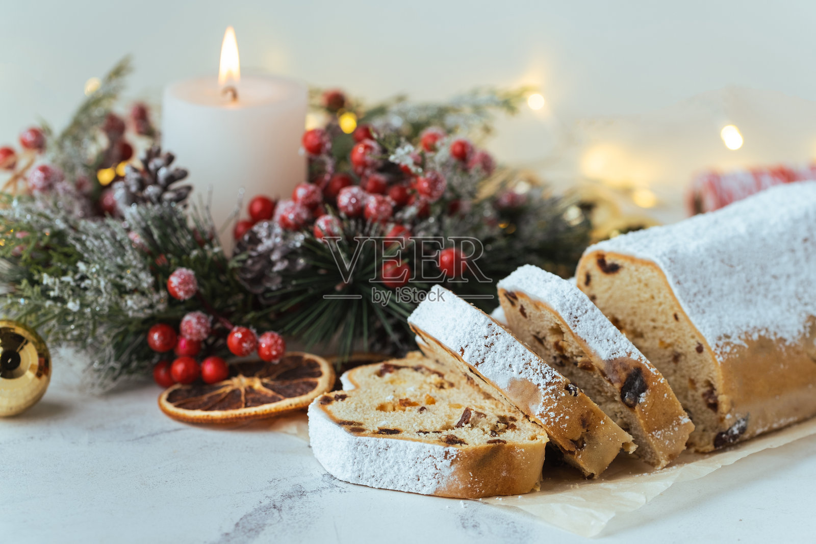 传统德国圣诞蛋糕斯托伦，内含葡萄干、水果和坚果，撒上糖粉，摆放在装饰有圣诞树枝、灯光和蜡烛的节日餐桌上。照片摄影图片