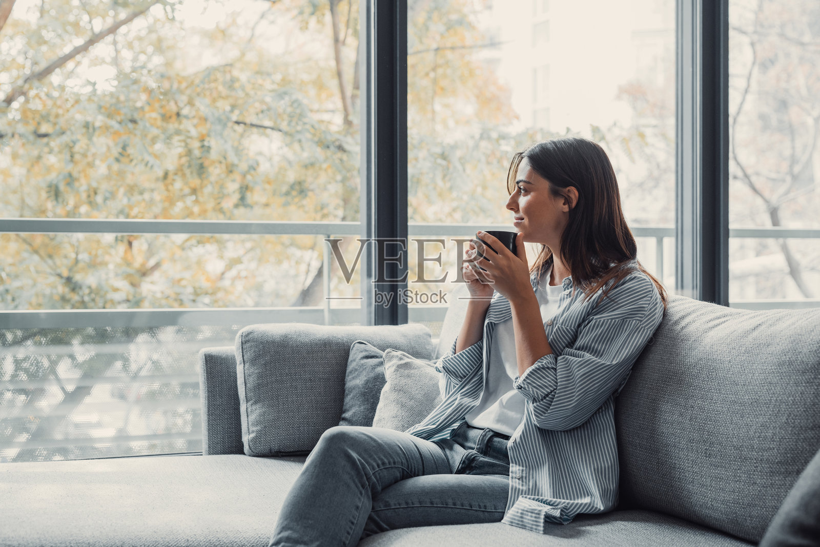 快乐的梦幻女孩手握热饮，目光投向远方，沉浸在美好的思绪中，微笑着，享受芳香的草本茶，闻着早晨的咖啡，温暖着双手。照片摄影图片