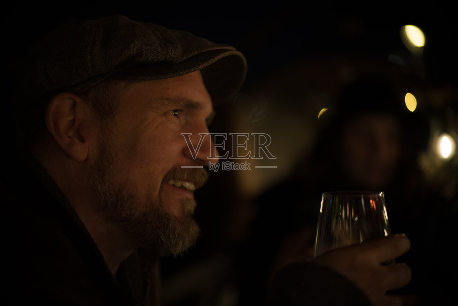 微笑的四十多岁有胡子的男人，脸颊高耸，戴着帽子，在浪漫的冬季晚餐中为他的第一次约会祝酒。照片摄影图片