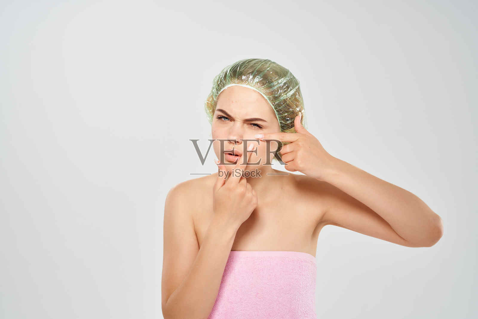 穿着粉色毛巾的女人在浅色背景下挤压脸上的黑点照片摄影图片