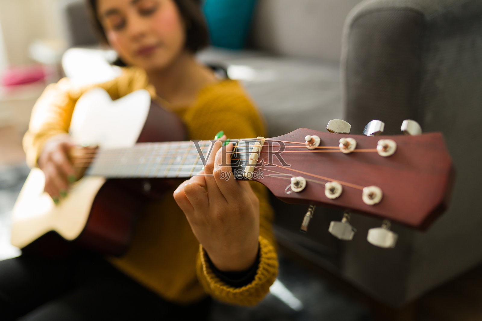 年轻女性坐在舒适的客厅里弹奏木吉他，专注于创作音乐，表达她的创意。照片摄影图片