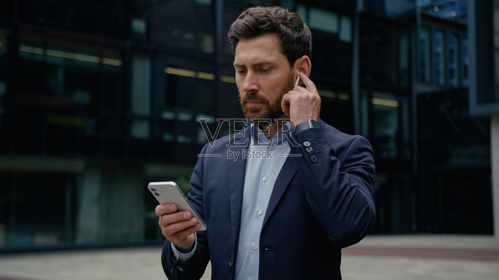 白人男性商人，成年企业家，男商业顾问，雇主，佩戴无线耳机在户外接听手机电话，使用智能手机与人交谈。照片摄影图片