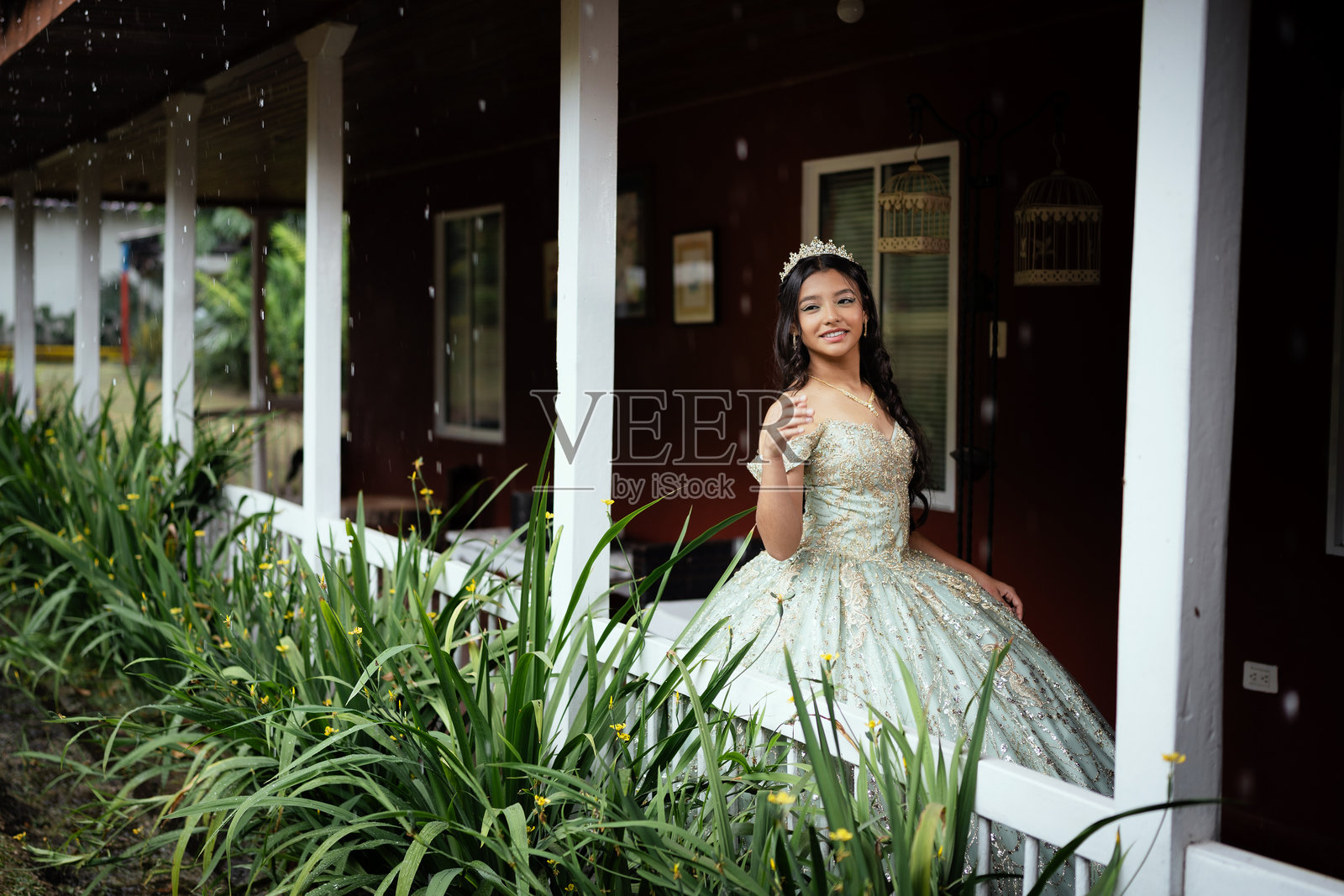 15岁少女穿着优雅的裙子，在十五岁生日庆典期间在门廊上摆姿势。照片摄影图片