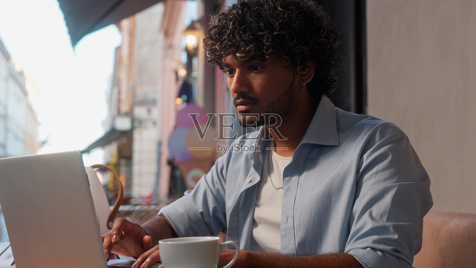 严肃的男性顾客、访客、客户、游客、旅行者在城市户外咖啡馆喝咖啡，印度阿拉伯男性正在网上预订酒店、下单购物，作为男性商人或学生进行远程工作，使用笔记本电脑。照片摄影图片