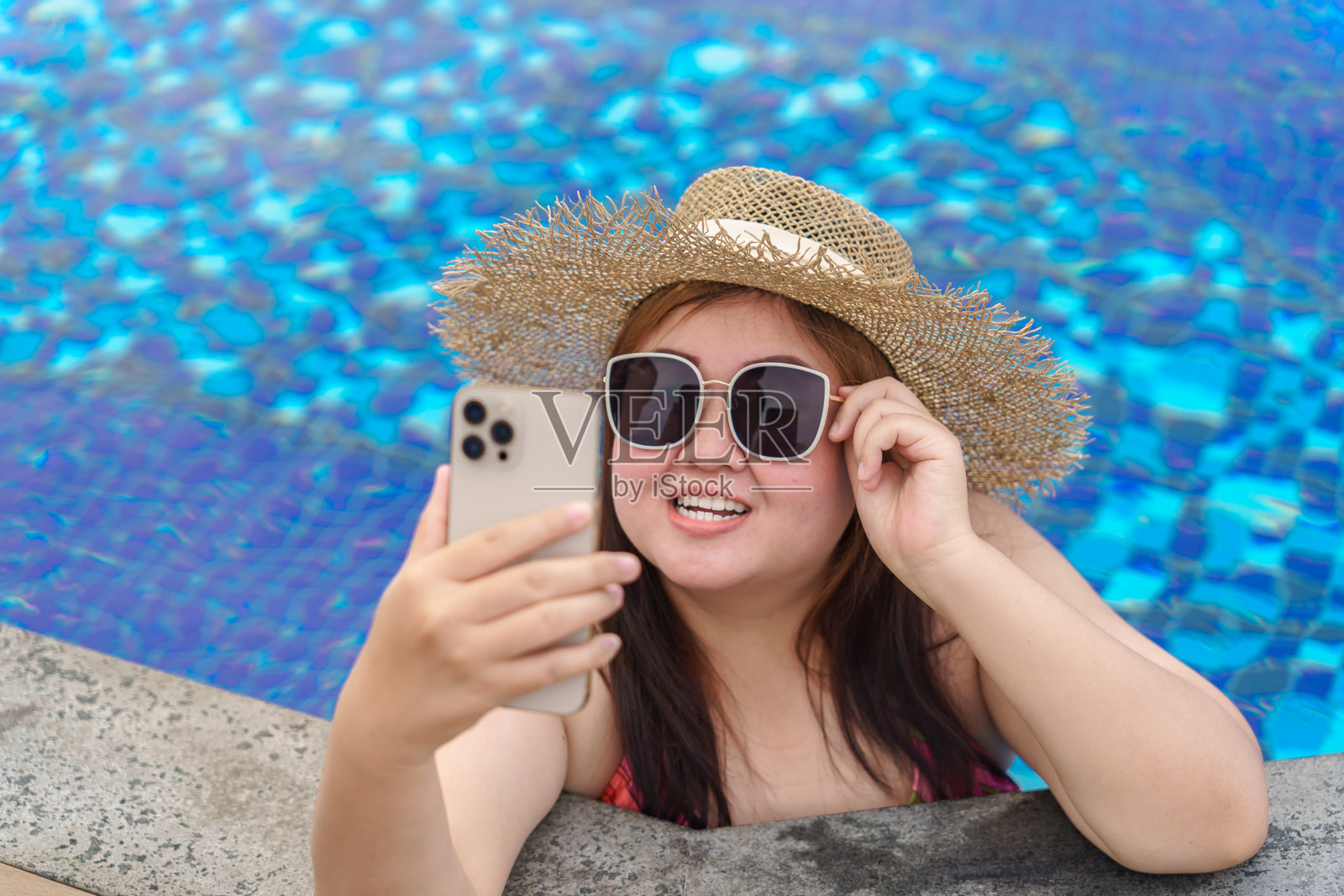 穿着橙色泳衣的年轻女性在游泳池中放松，手里拿着智能手机。肥胖女性度假旅行，手中使用手机。照片摄影图片