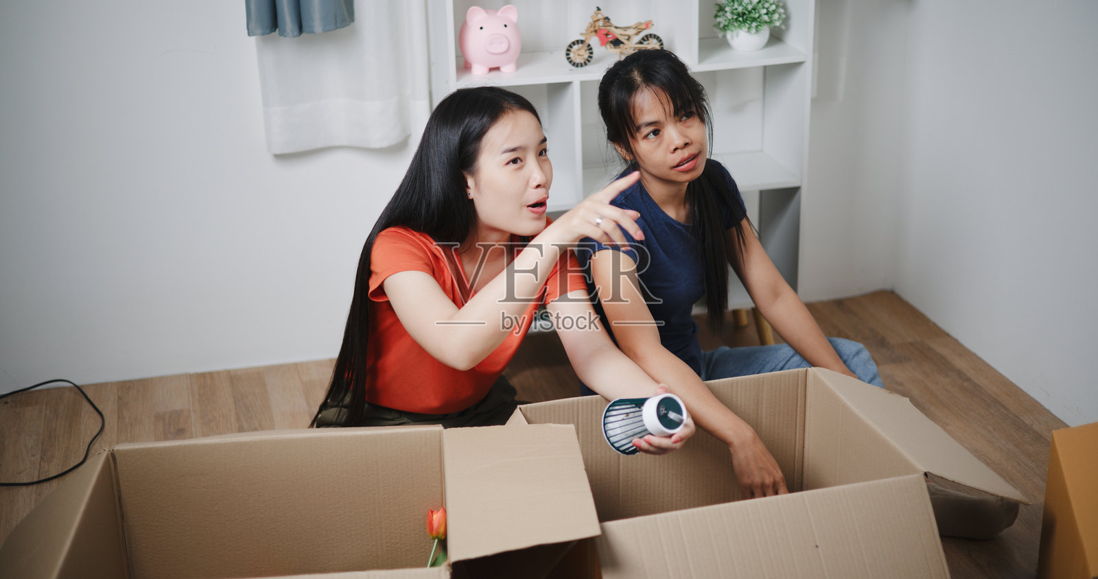 两位快乐的亚洲女性正在帮助装饰她们的客厅书架。照片摄影图片