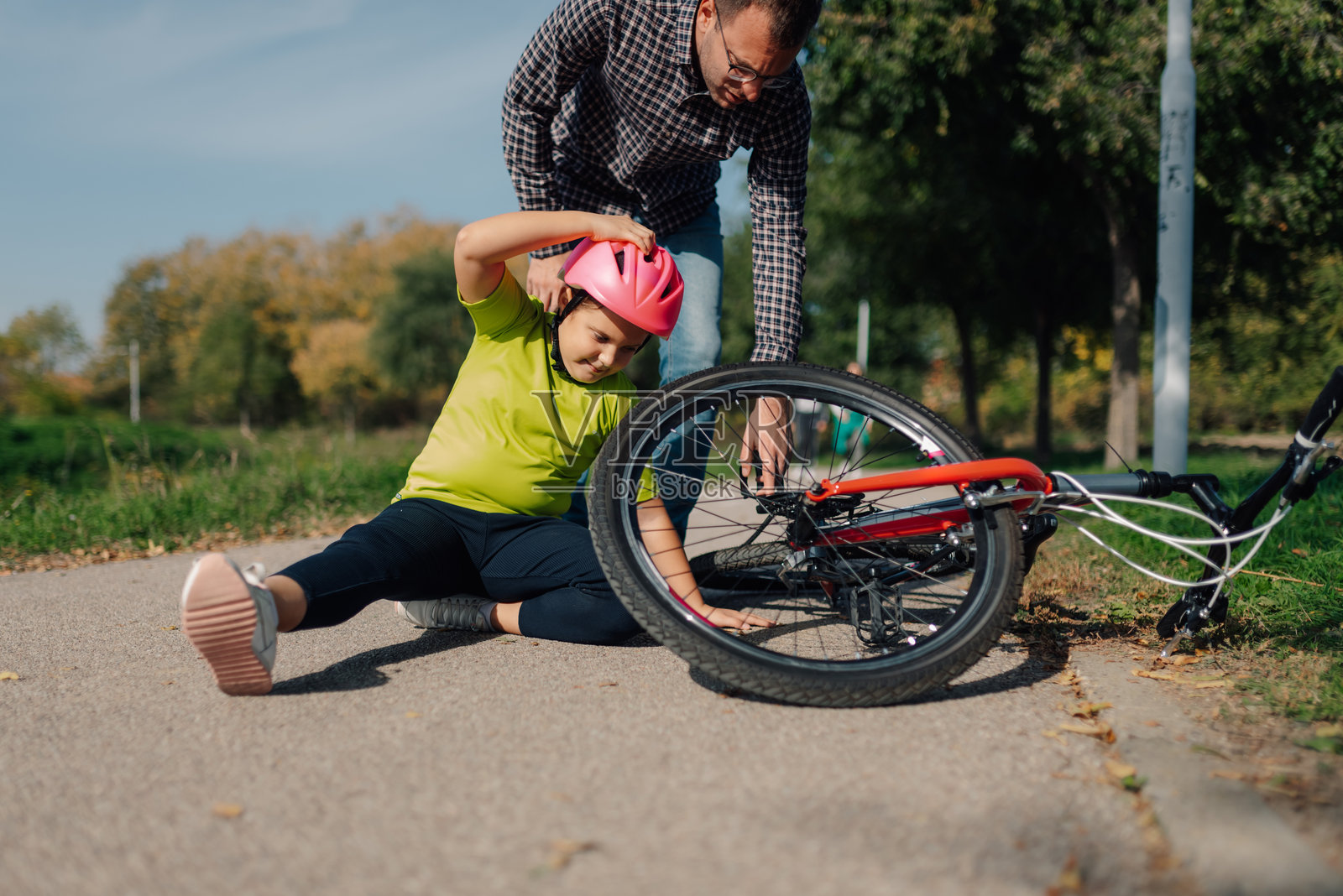 父亲在公园里帮助女儿处理自行车事故后事宜照片摄影图片