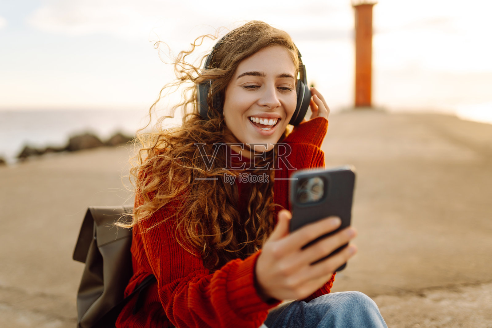 放松的女性在灯塔旁的水边享受音乐，戴着耳机。照片摄影图片