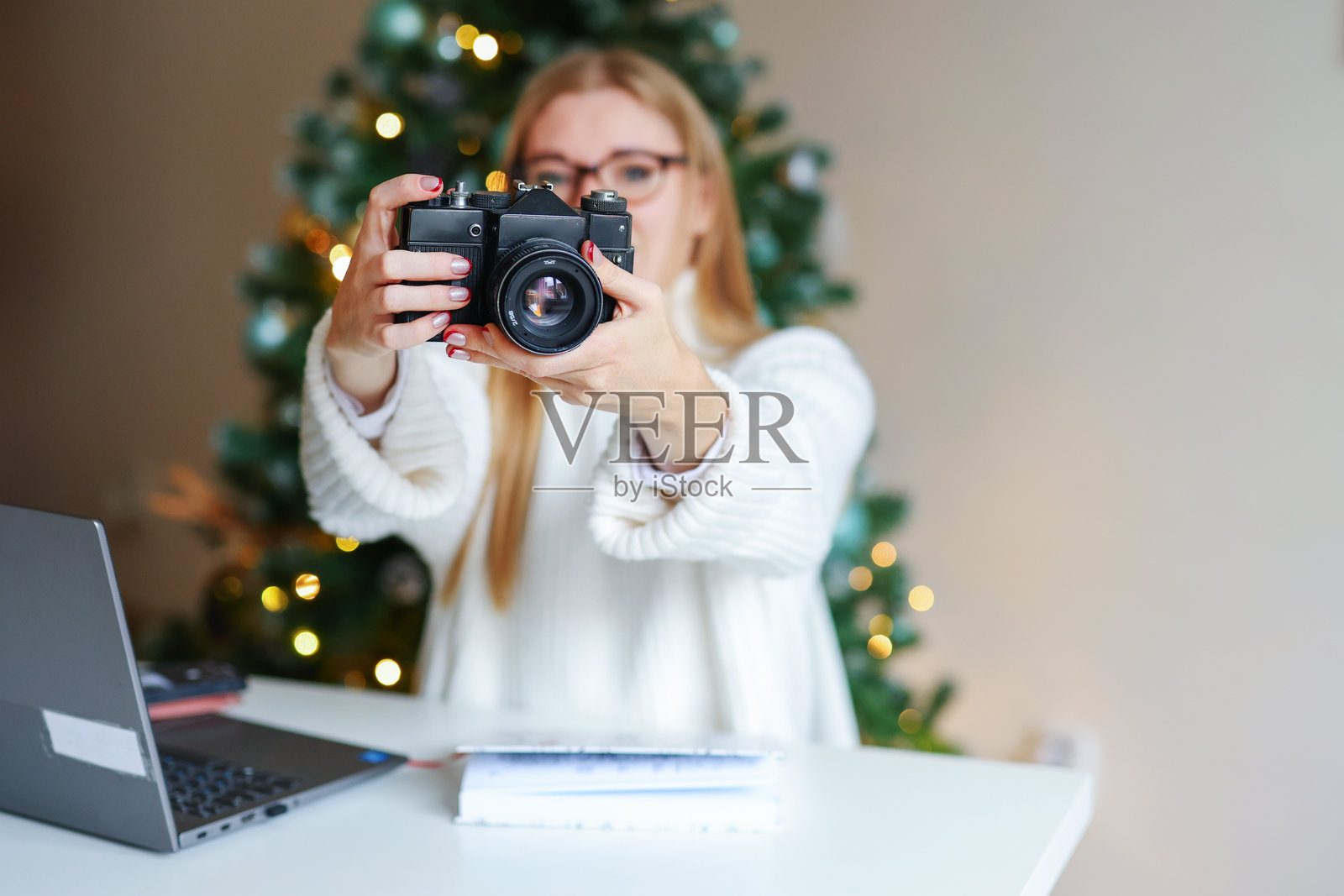 女孩在圣诞树背景下手持相机。留白空间。照片摄影图片