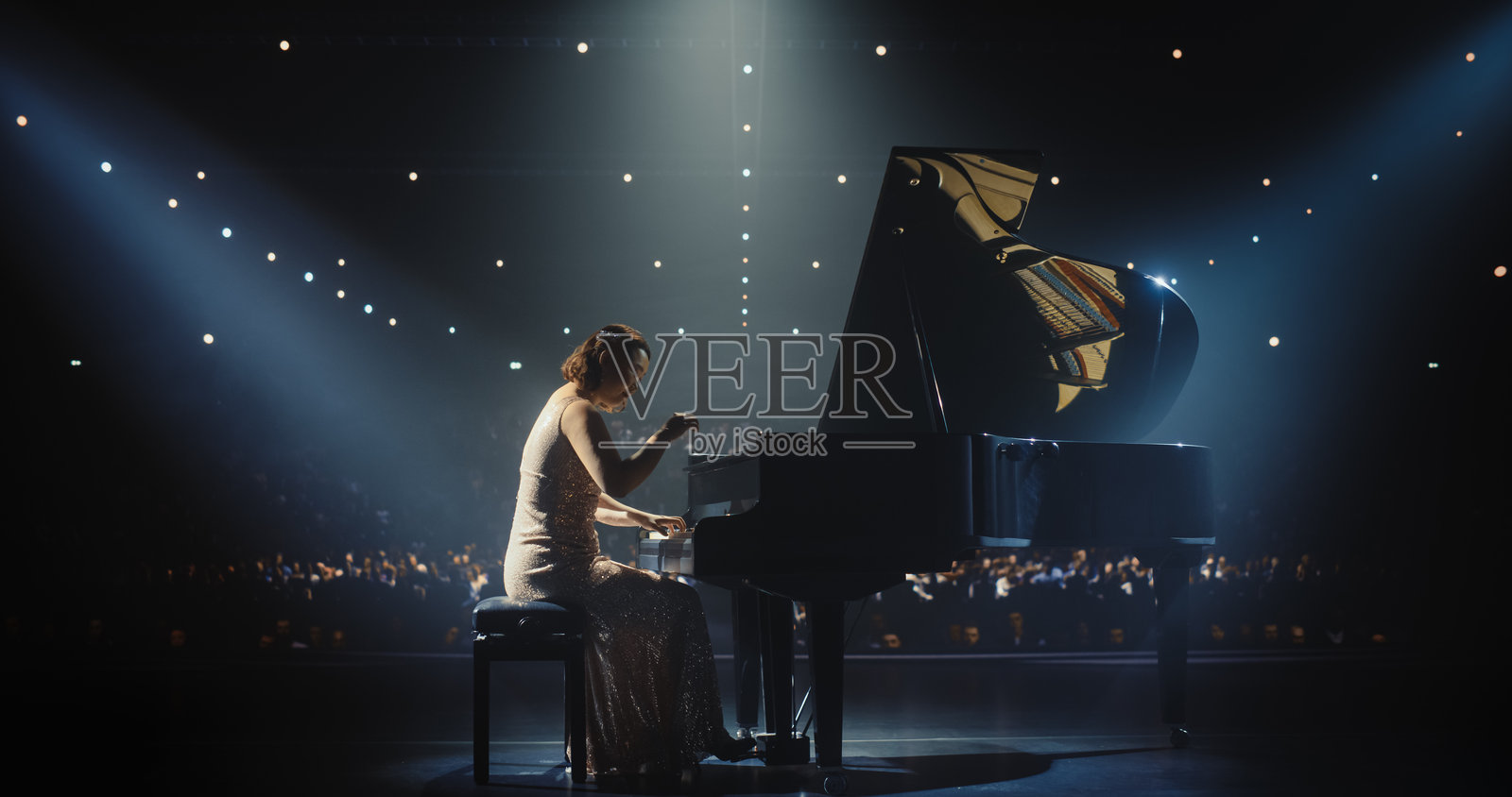 女作曲家倾注灵魂于大钢琴，优美的音符充盈整个场馆。舞台灯光营造出宁静的氛围，增强了她古典表演的情感深度。照片摄影图片