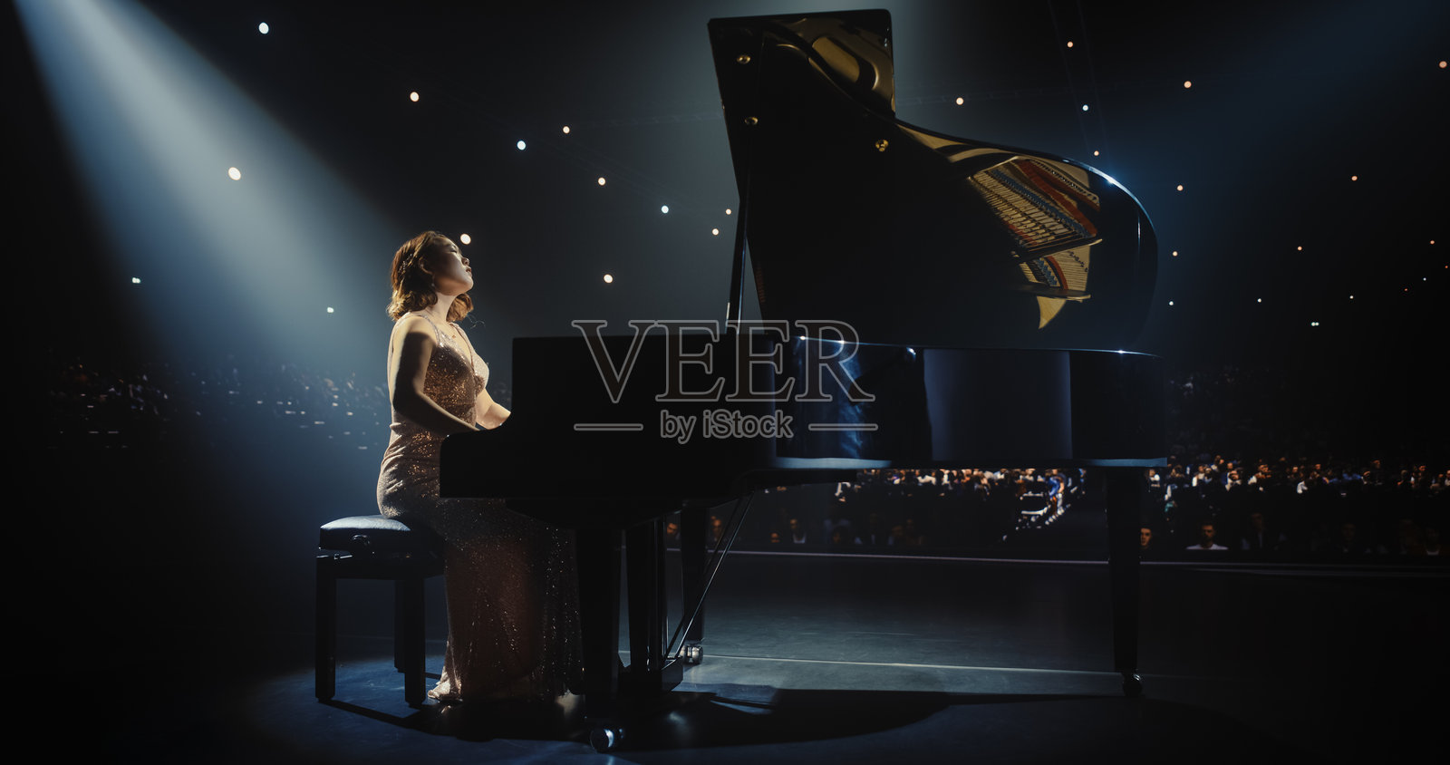 一位才华横溢的亚洲钢琴家在大钢琴上进行精彩的表演，吸引了观众的目光。在柔和的舞台灯光下，她的手指在琴键上灵活移动，演奏出优美的古典音乐。照片摄影图片