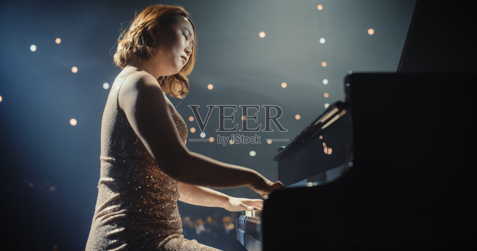 古典钢琴音乐会：在聚光灯下，亚洲女钢琴家在大钢琴上演绎出强劲的表演。优雅的舞台布置衬托出她充满激情的演奏。照片摄影图片