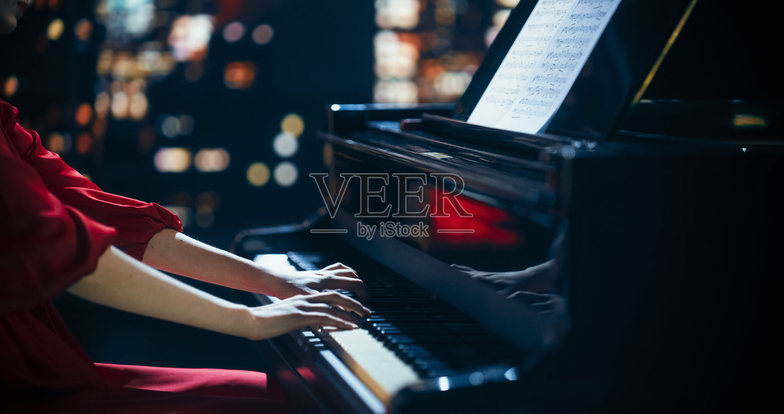 特写镜头下，一位才华横溢的匿名钢琴家在大钢琴上进行精彩的演奏。在柔和的舞台灯光下，女性的手指在琴键上灵活移动，演奏出优美的古典音乐。照片摄影图片