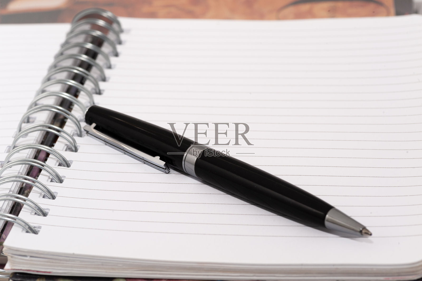 一本螺旋装订的笔记本上放着一支黑色的笔，白色的页面上清晰可见。照片摄影图片