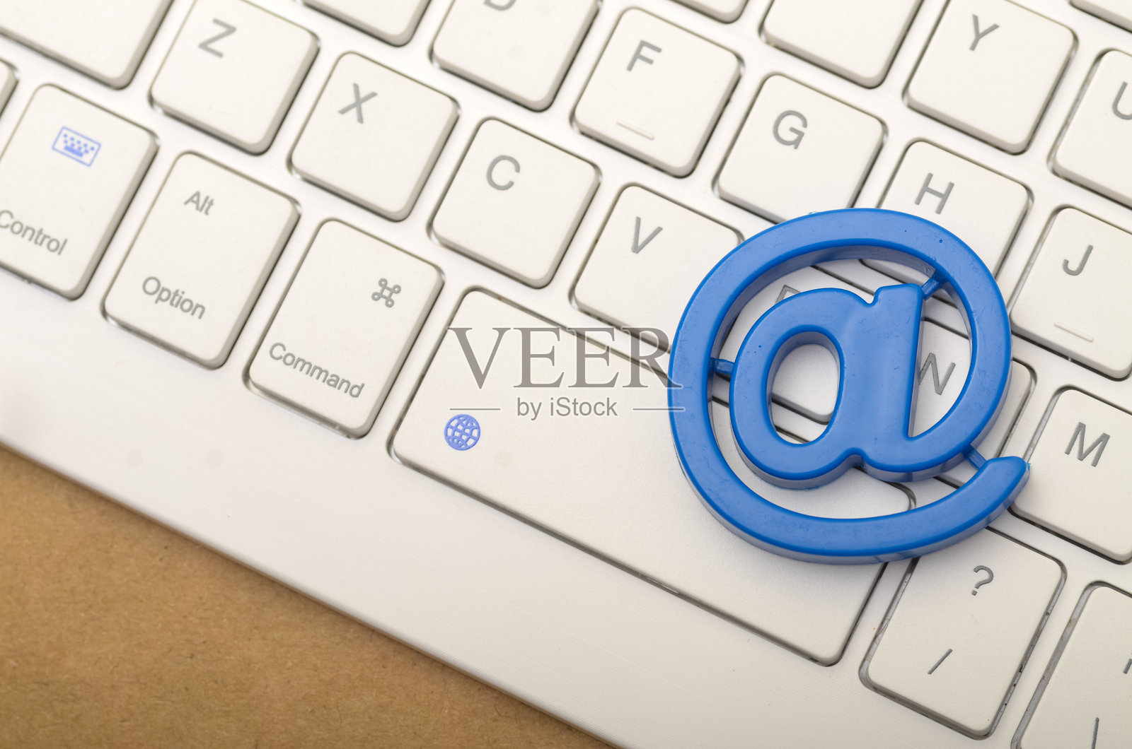 一个蓝色塑料@符号放在白色电脑键盘上，突显了电子邮件在现代沟通中的重要性。照片摄影图片