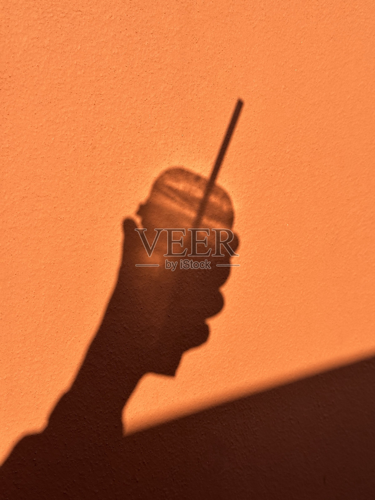 手握饮料的手在橙色墙壁上投下阴影照片摄影图片