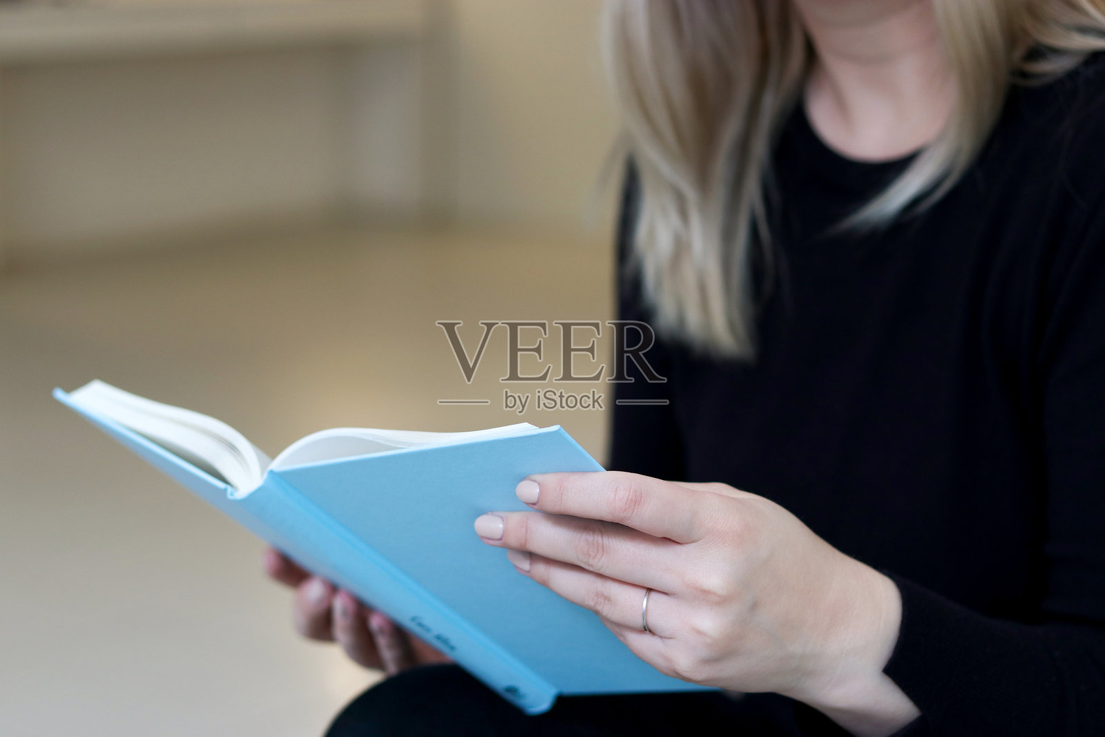 一位金发女性坐在沙发上，手中拿着一本蓝色的样本书的特写肖像。照片摄影图片