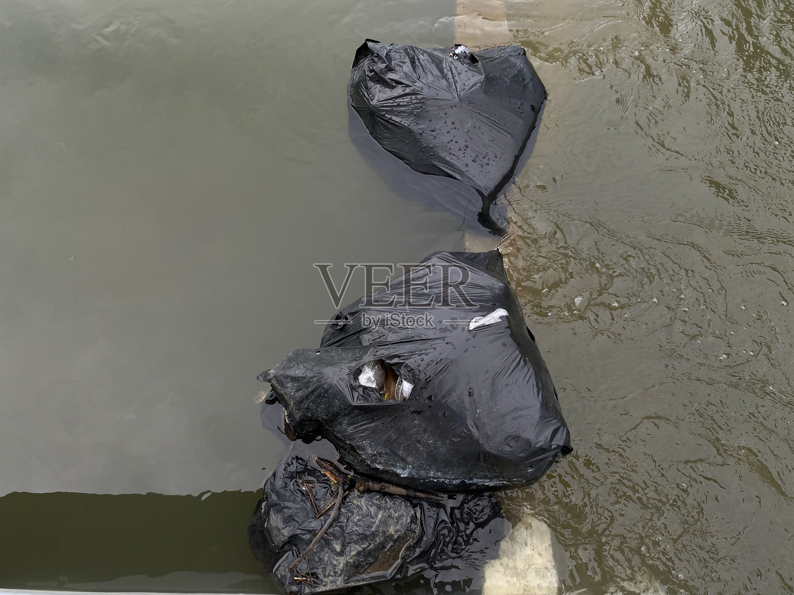河水溢出，穿过黑色垃圾袋，导致街道上发生洪水。照片摄影图片