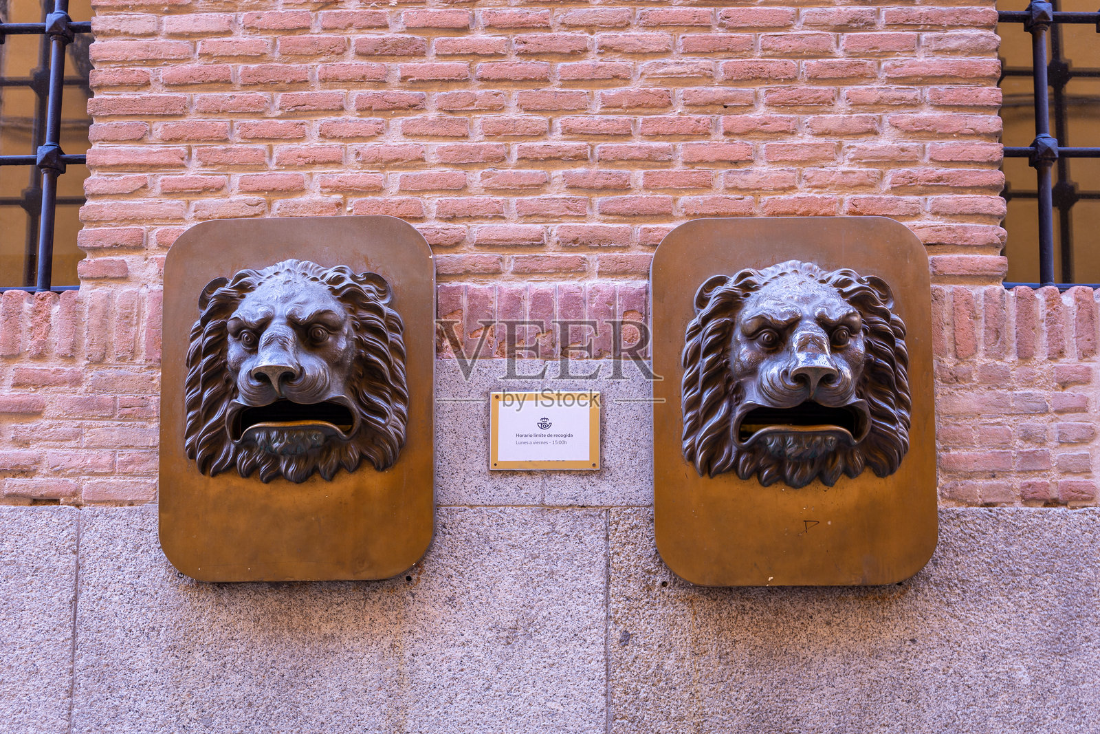 西班牙托莱多砖砌建筑外立面上的两个青铜狮头雕塑邮筒。照片摄影图片