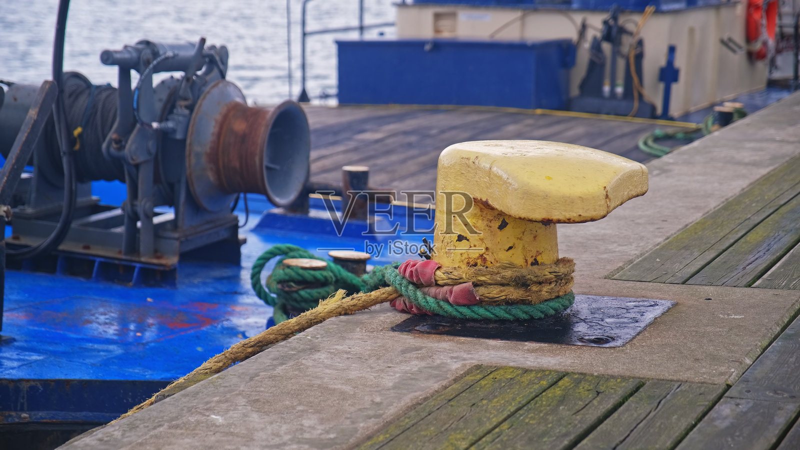 工业海事工程船只停靠在港口码头，周围用聚丙烯尼龙塑料绳缠绕在黄色金属系船柱上。照片摄影图片