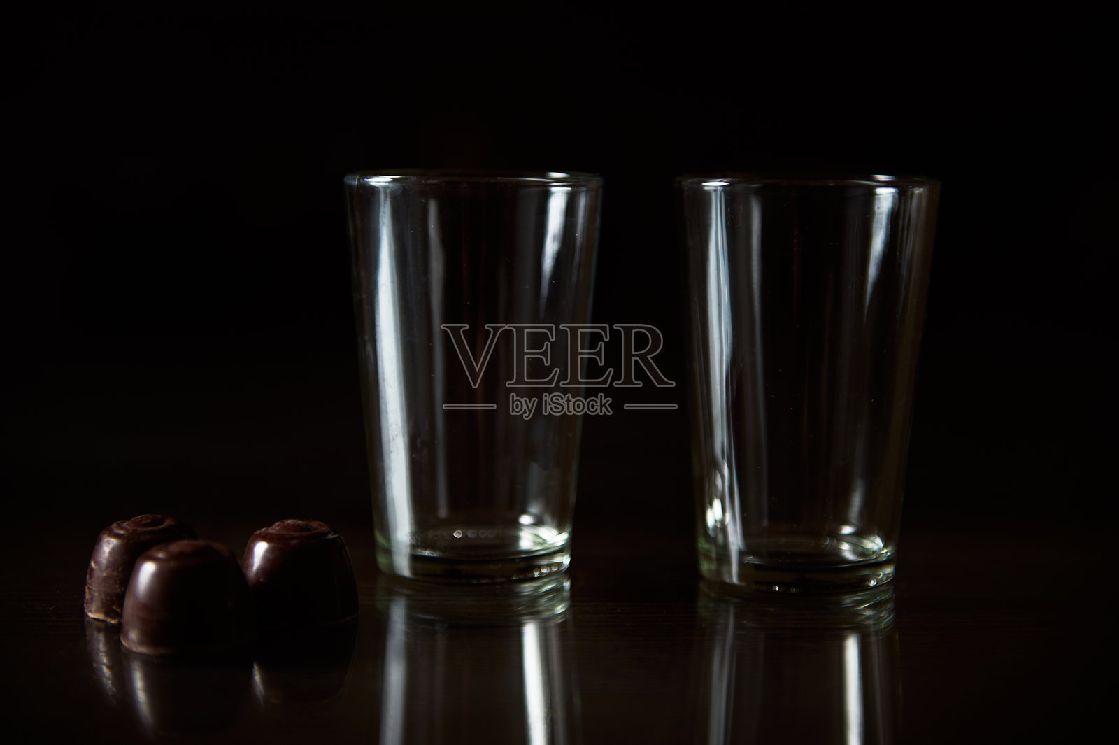 两个空玻璃杯和巧克力放在黑色反光表面上照片摄影图片