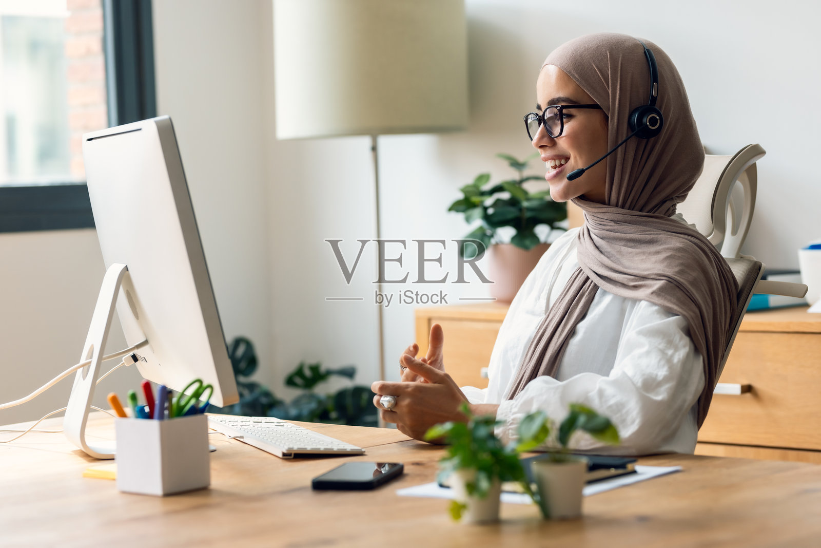 年轻女商人在办公室用耳机与电脑进行视频通话照片摄影图片