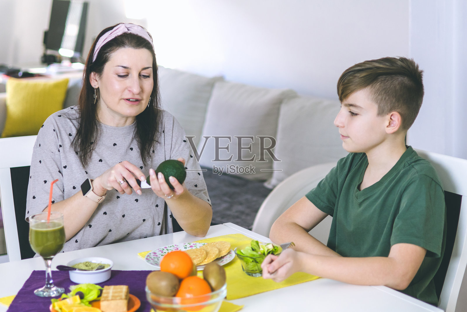 母亲和儿子在家中享受准备健康早餐的时光。早餐的超级食品成分包括螺旋藻、熏豆腐、鳄梨、生菜、米饼和水果。照片摄影图片