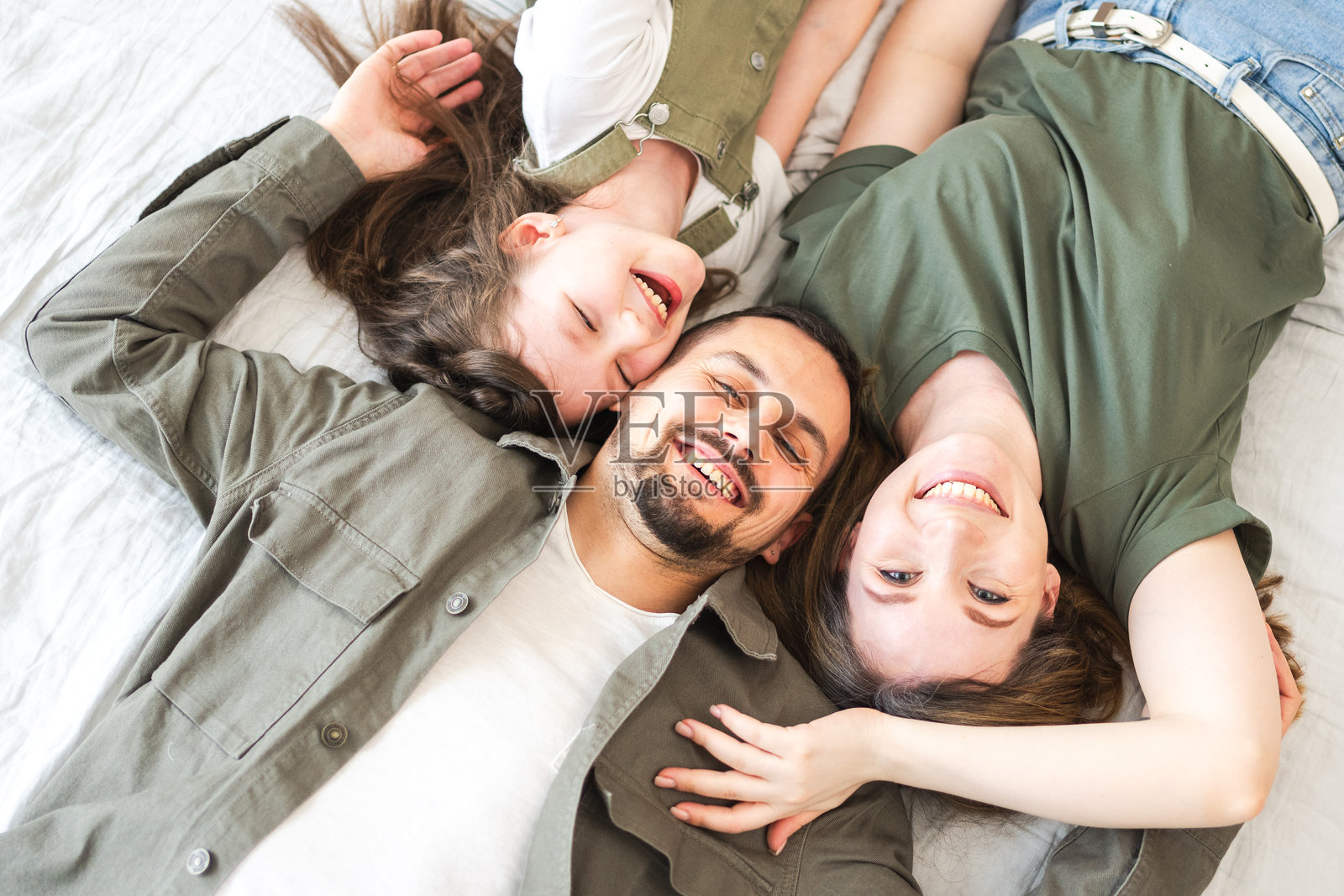 快乐的家庭在家中。母亲、父亲和孩子们在室内的床上放松，妈妈和爸爸与女儿一起玩耍、拥抱，享受快乐的时光。家庭成员微笑、欢笑，享受温馨的时刻。照片摄影图片