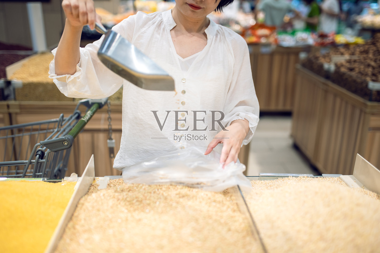 一位亚洲女性在超市用勺子将新鲜面粉和豆子放入纸袋中。照片摄影图片