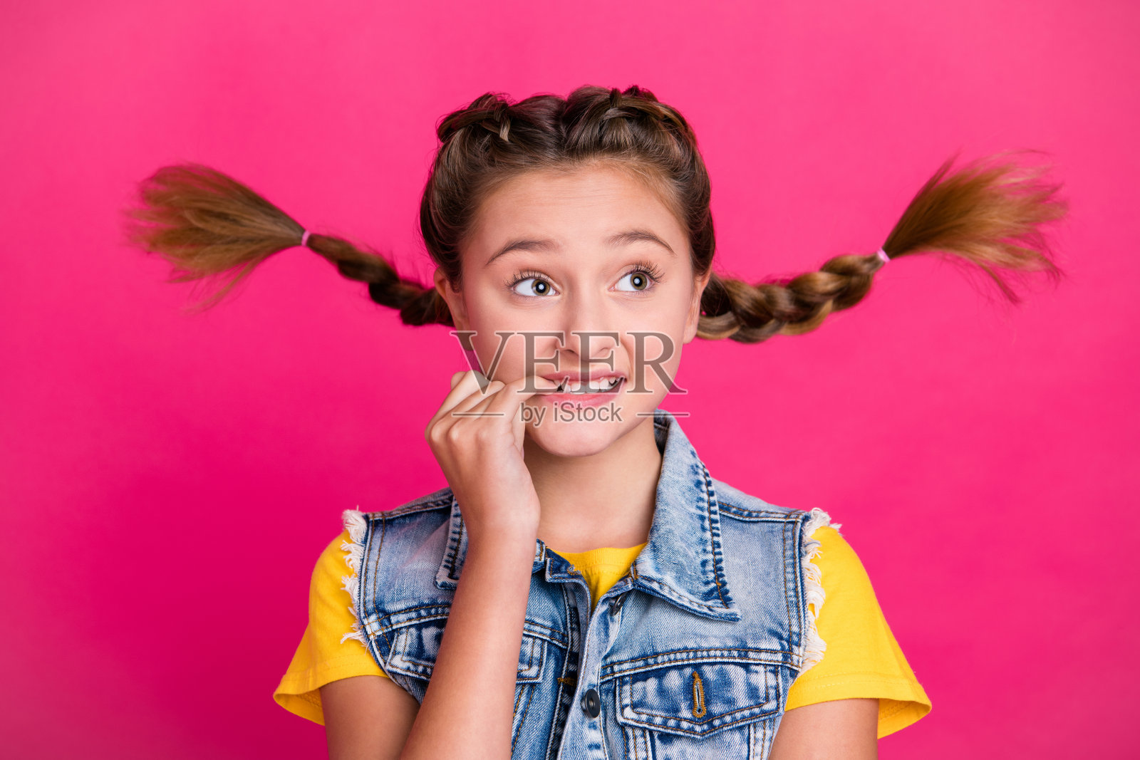 害怕的小金发女孩穿着T恤、牛仔裤和背心，望向空旷的空间，背景色彩鲜艳。照片摄影图片