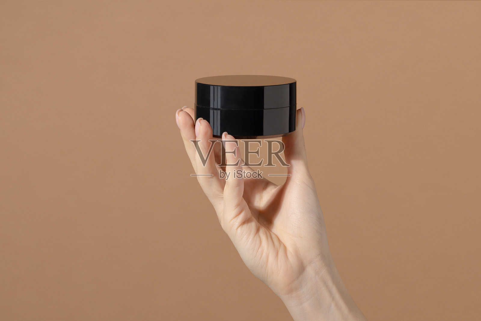 女人手掌上的特写镜头，黑色塑料制成的保湿霜瓶子，背景为棕色。无标签的瓶子模拟图，包含抗衰老面膜和美容磨砂膏。护肤概念。照片摄影图片