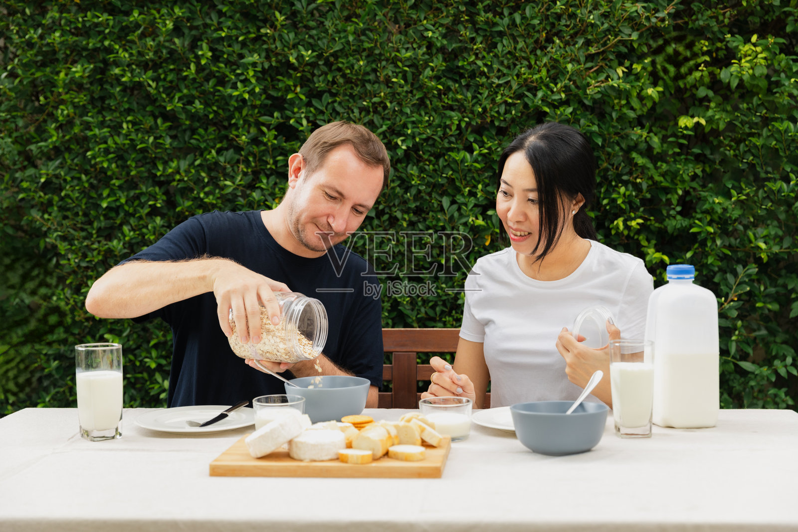 一对情侣在宁静的花园环境中享受健康的早餐，倒燕麦并分享微笑，晨光熹微。照片摄影图片