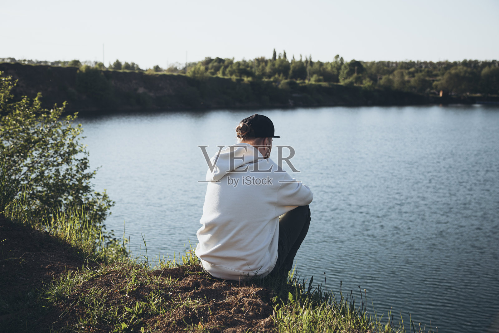 A man sits in front of a lake in the mountains and enjoys the view.照片摄影图片