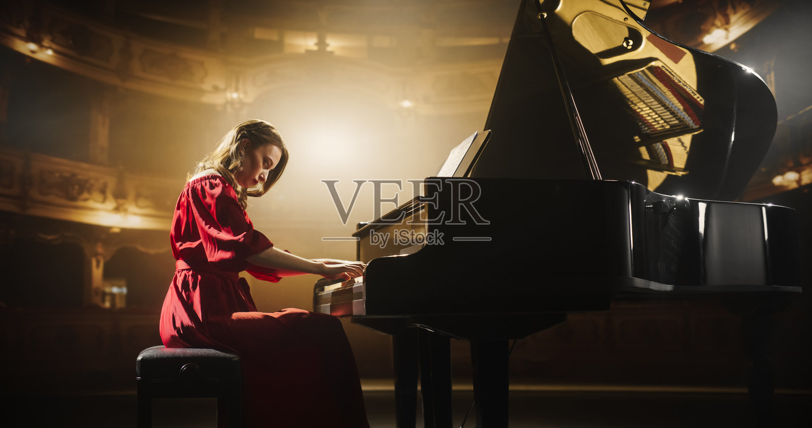 在明亮的金色音乐会舞台上，女钢琴家在大钢琴上演奏情感丰富的即兴曲。每一个音符在音乐厅中回响，激动着观众。聚焦于双手。照片摄影图片