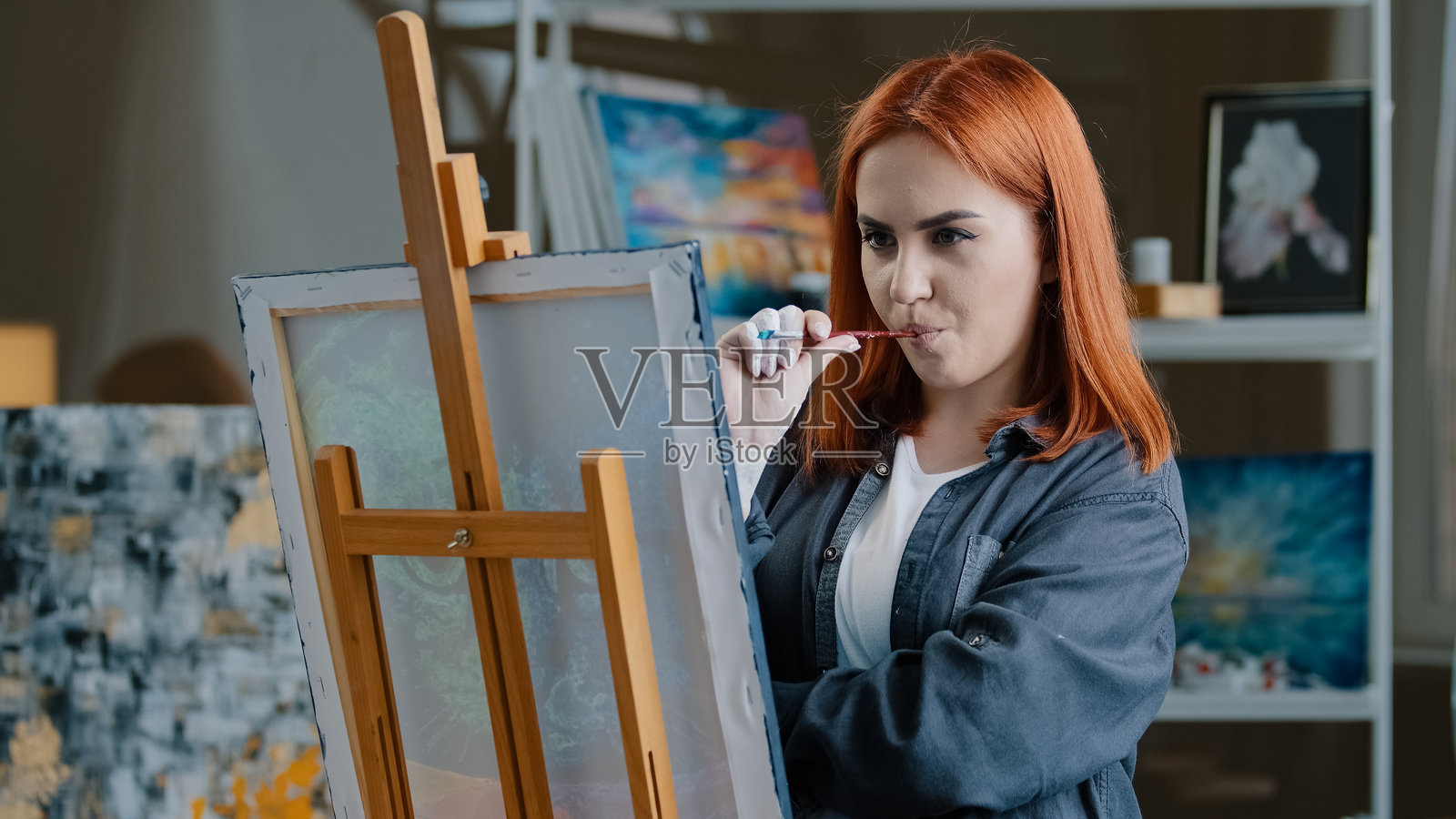 沉思的红发白人女性在房间里绘画，思考创作画作的想法，沉浸于绘画爱好，才华横溢的女孩在画布上用丙烯颜料创作当代艺术作品。照片摄影图片