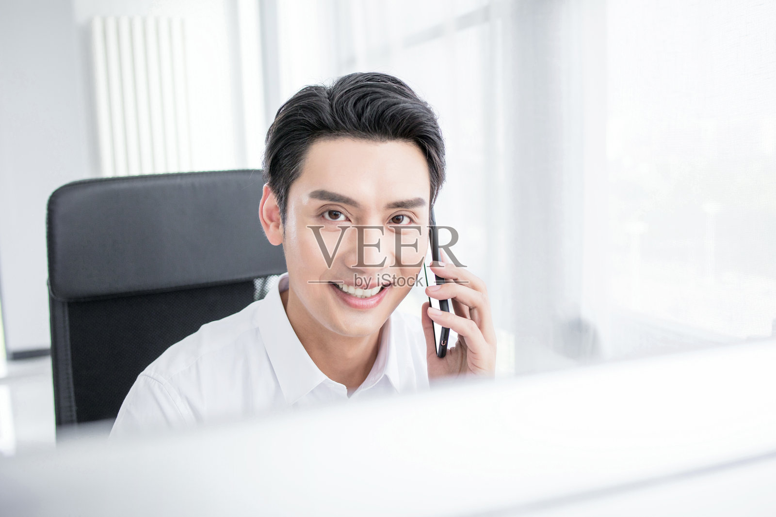 年轻帅气的商人在现代办公室的桌子上使用笔记本电脑，正在打电话，具备良好的计划和组织能力，年收入可观，致力于推广和营销业务。照片摄影图片