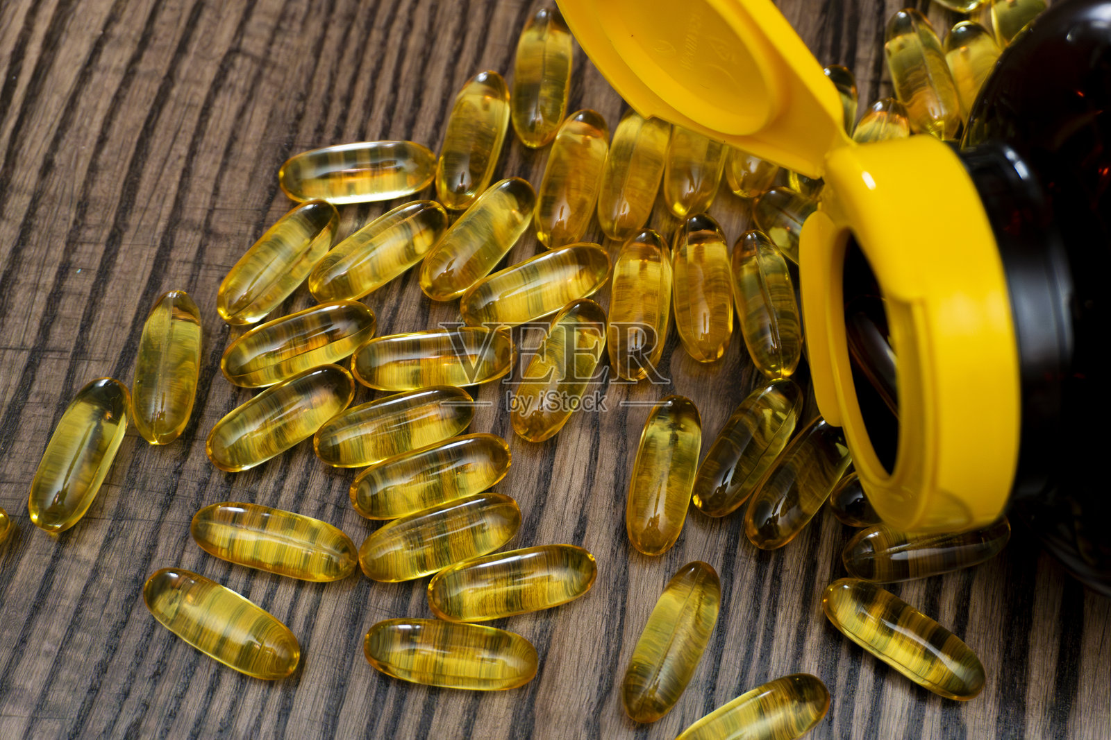 黄色胶囊从一个打开的瓶子中洒落在木质表面上照片摄影图片