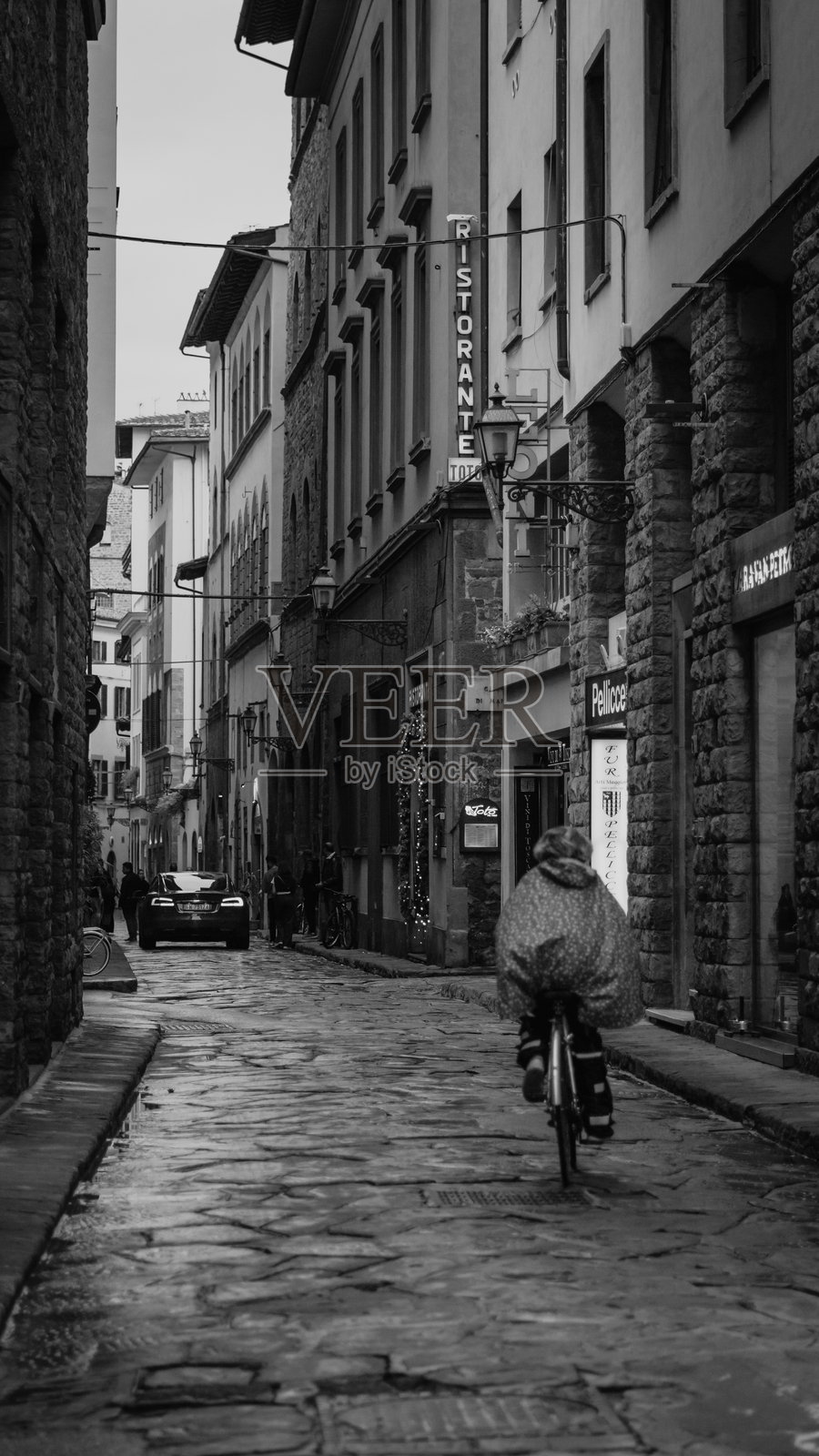 骑自行车的人在佛罗伦萨老城的雨中穿行。照片摄影图片