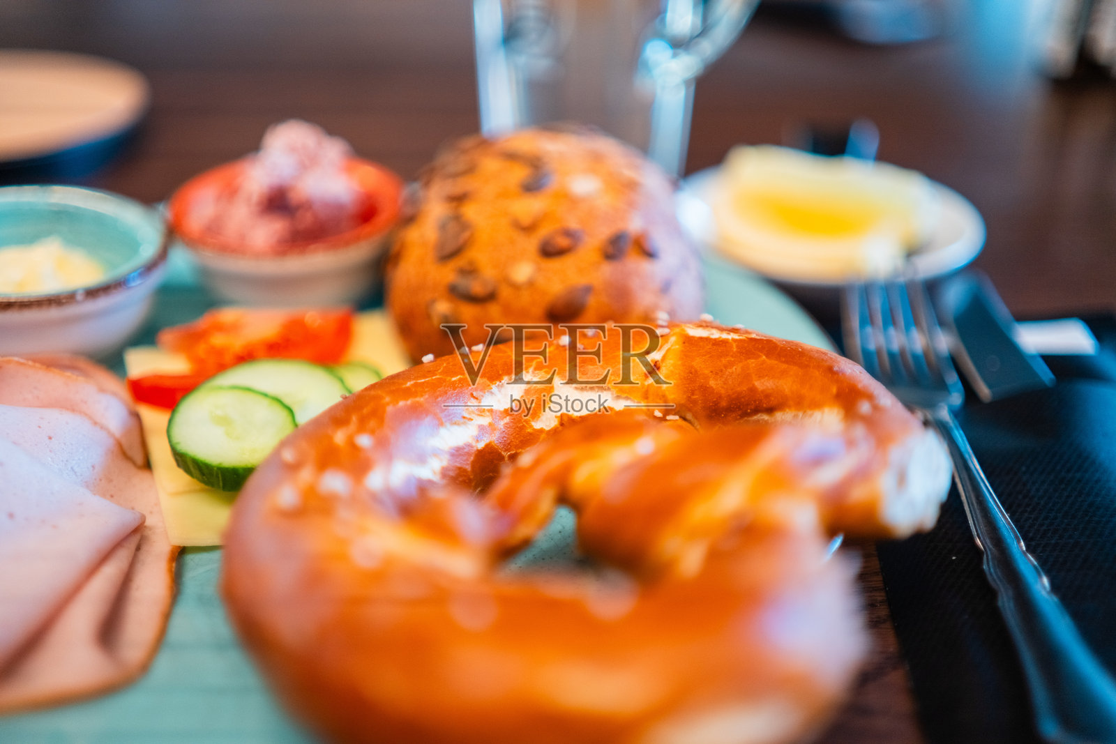 美味的早餐盘，配有新鲜的椒盐卷饼、冷切肉和蔬菜，在自然光照射下的乡村木桌上提供愉悦的早晨体验。照片摄影图片