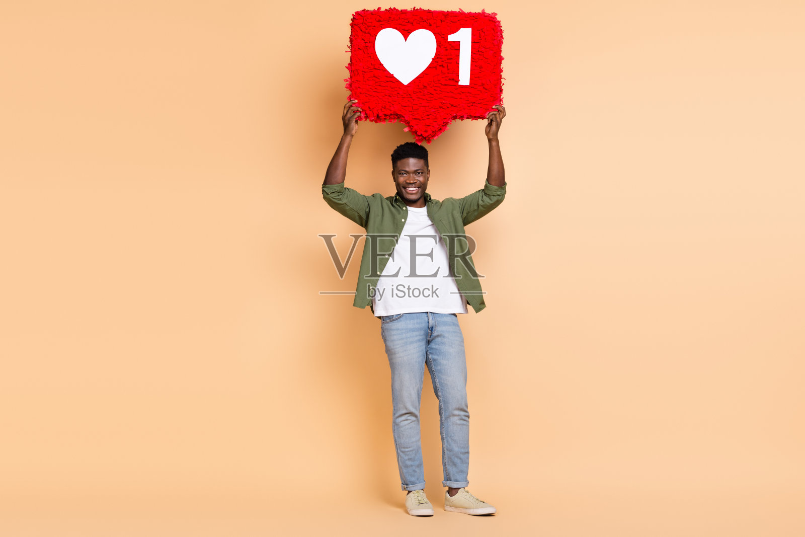 男孩手持纸质心形皮纳塔，穿着牛仔衬衫和牛仔裤，背景为柔和的色彩，像是在鼓励关注和订阅博客。照片摄影图片