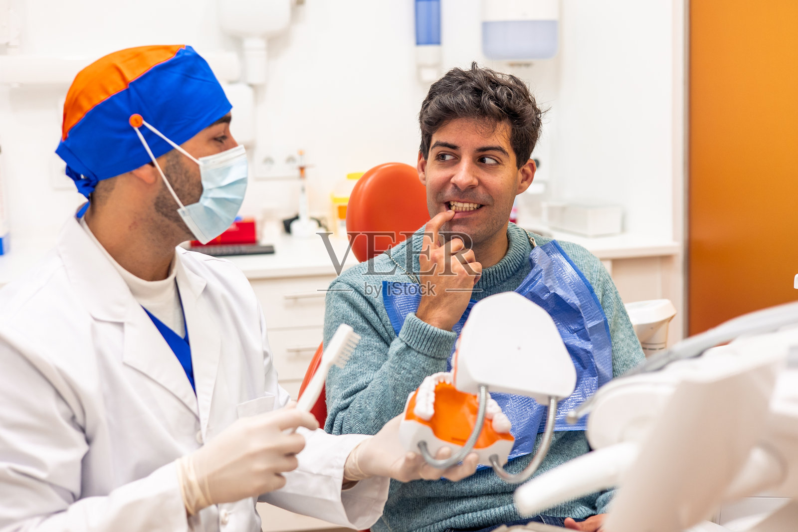 牙医向患者展示正确的刷牙方法，使用牙刷和颌骨模型。照片摄影图片