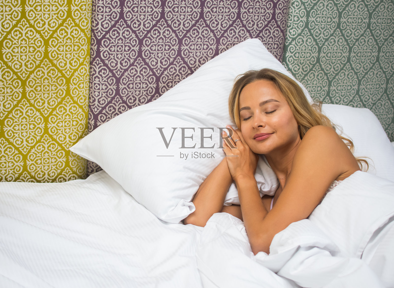 年轻女性安静地躺在白色床单和图案床头板的床上睡觉照片摄影图片
