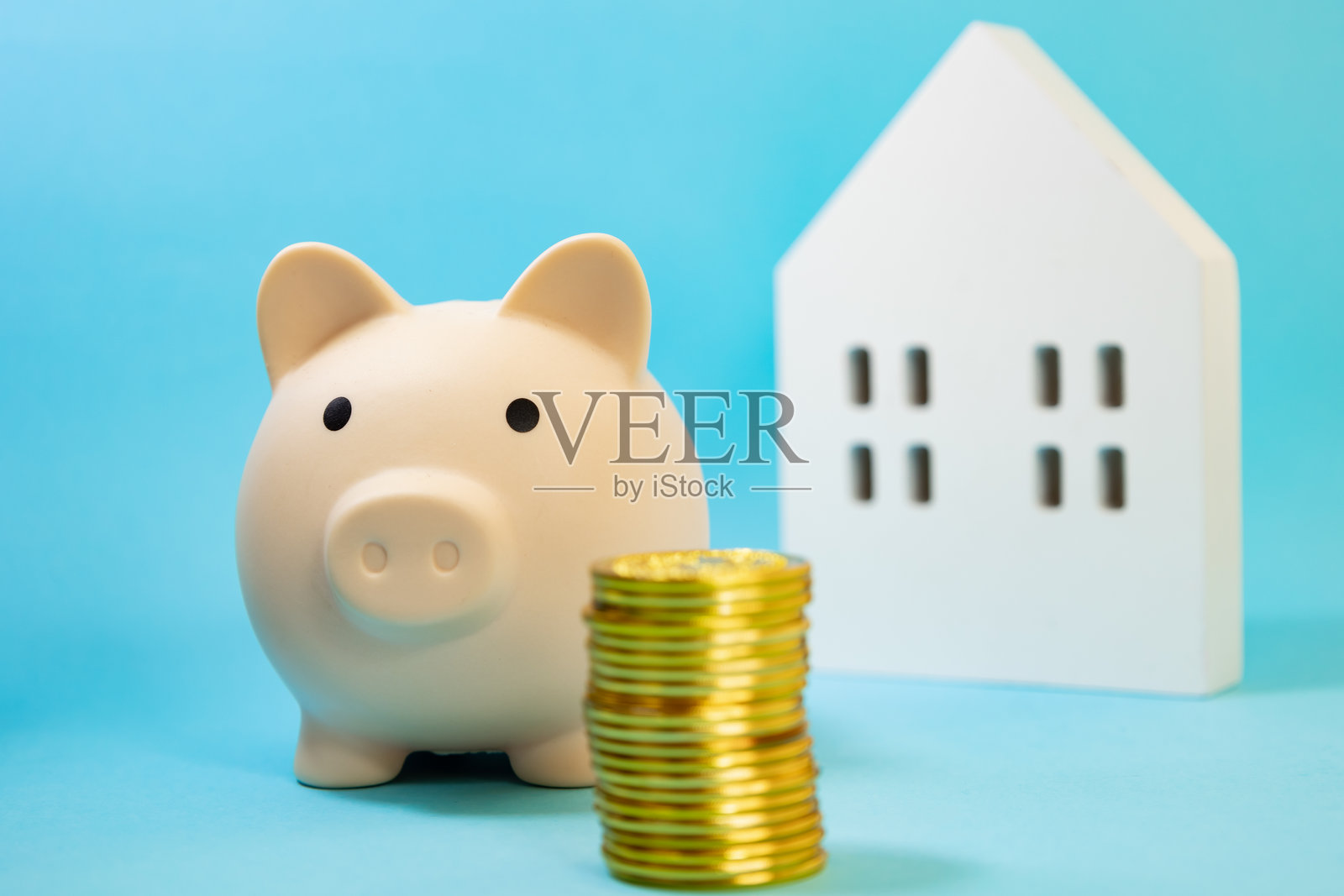 蓝色背景下，旁边放着叠好的金币的储蓄罐，背后模糊的房子。照片摄影图片