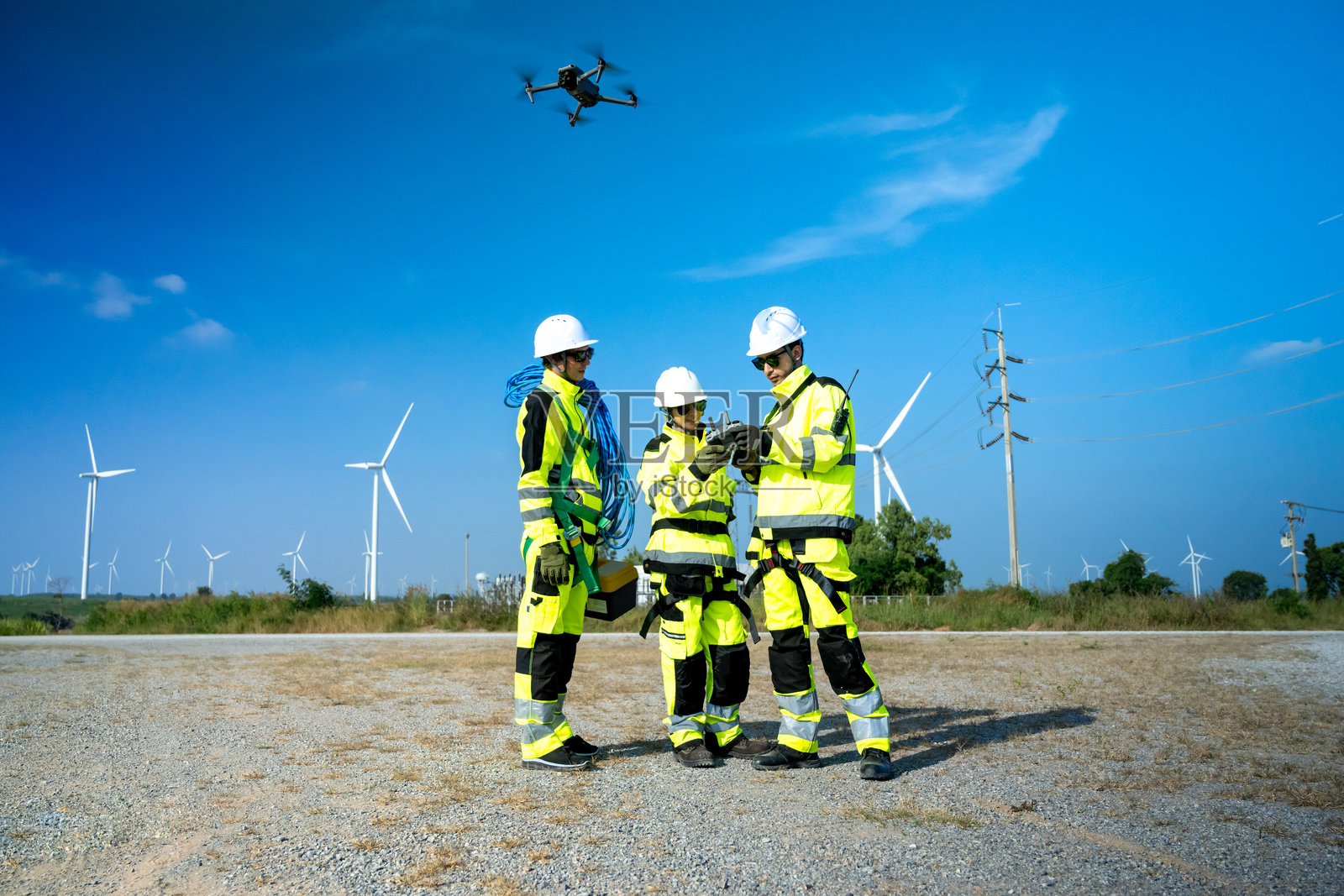 一名戴着安全帽和安全背心的工程师操作无人机检查偏远地区高耸的风力涡轮机。照片摄影图片