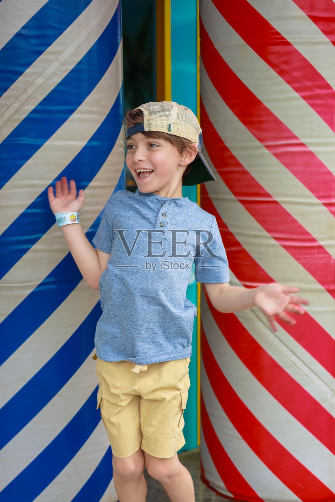 男孩戴着帽子和手环，兴奋地站在五彩斑斓的条纹柱子之间。照片摄影图片