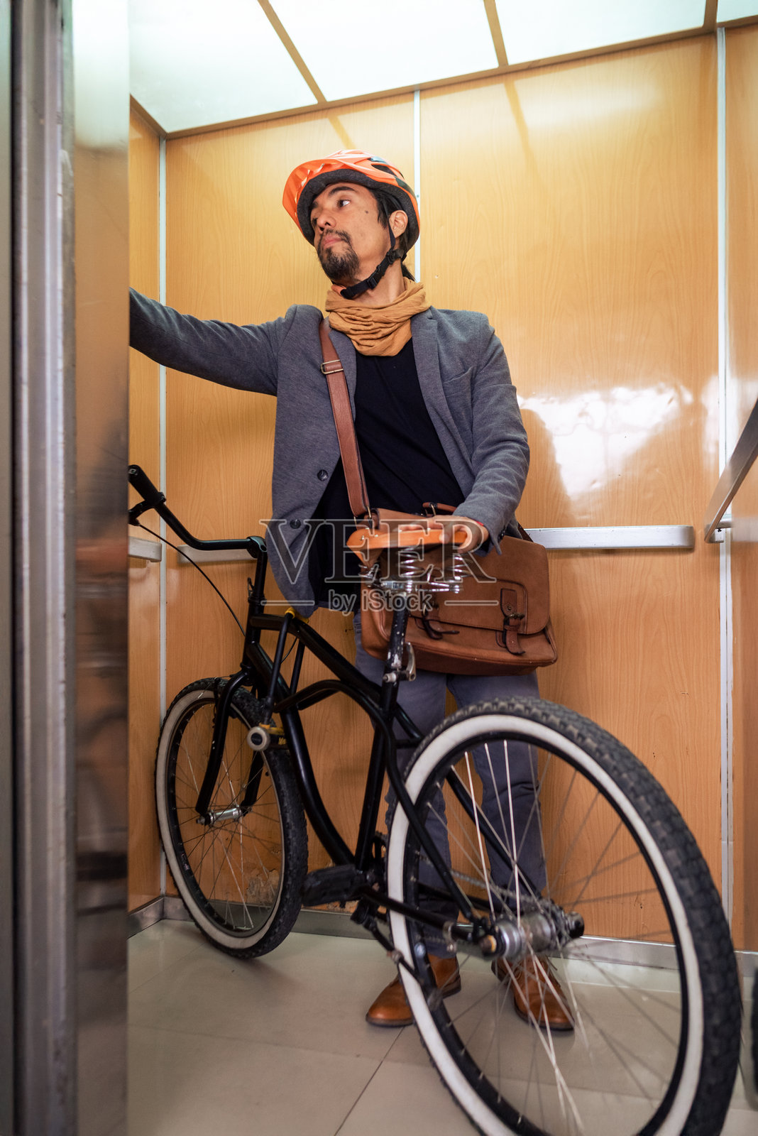 一位商人在电梯内与他的自行车一起，正在按按钮的竖直图像。照片摄影图片