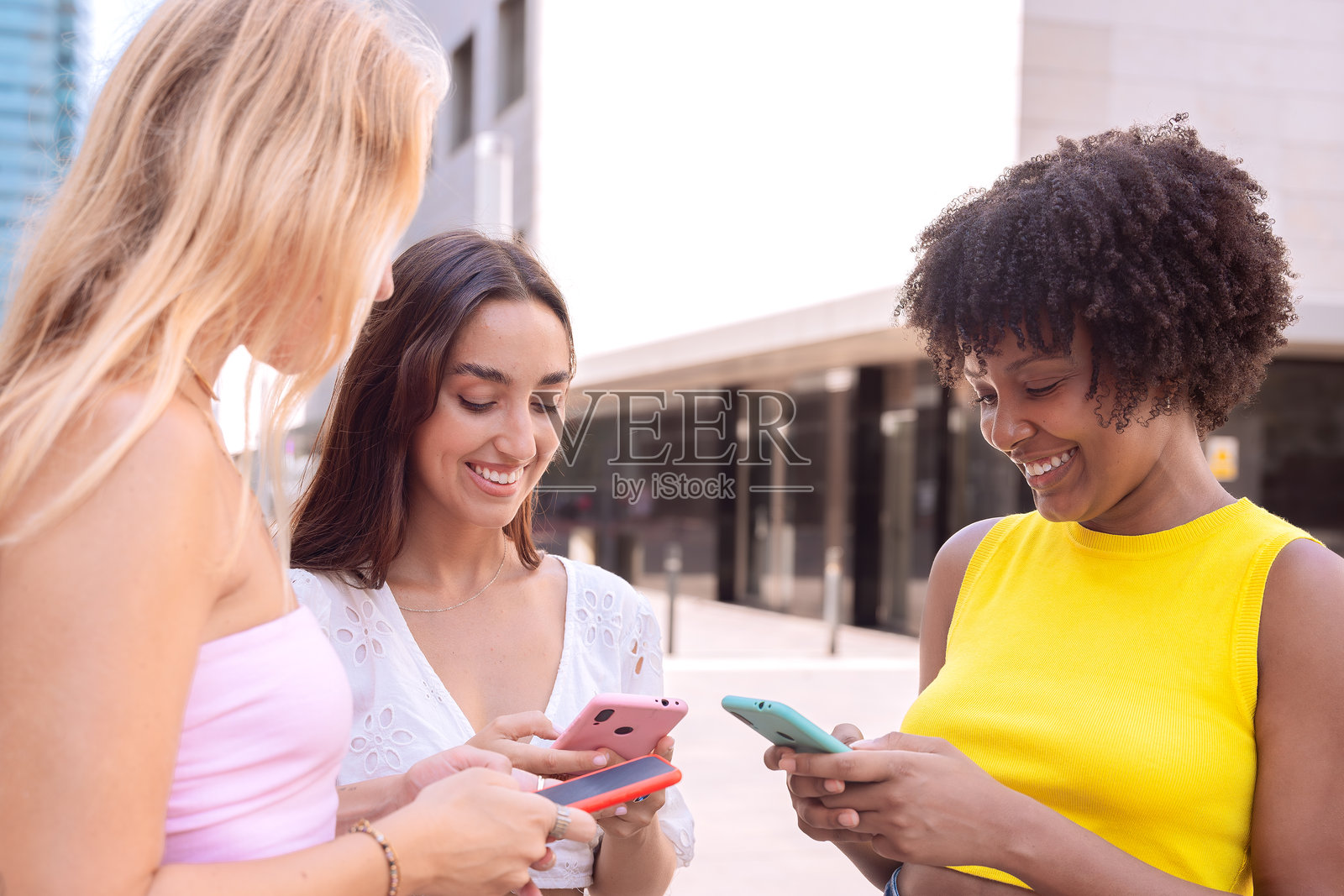 三个兴奋的朋友在户外看着智能手机。照片摄影图片