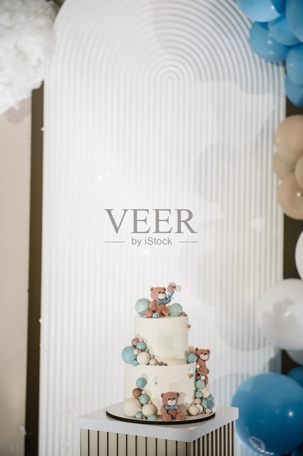 美味的接待。时尚的生日蛋糕，上面有小熊造型，适合1、2、3岁的小男孩特写。照片墙装饰有棕色、蓝色和金色气球。庆祝洗礼的概念。生日派对。照片摄影图片